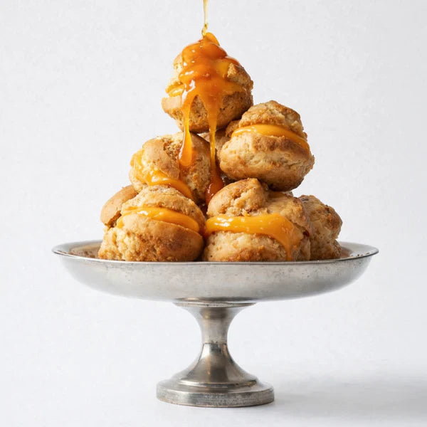 Stack of golden brown pastries with caramel sauce on a silver pedestal dish against a white background