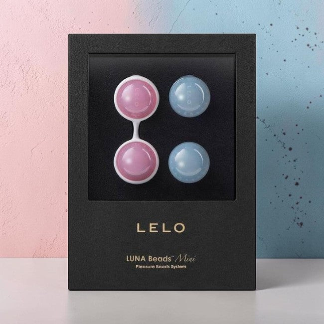 LELO Luna Beads Mini package containing four small round beach beads, two pink and two light blue, displayed inside a black box against a split pastel pink and blue background.