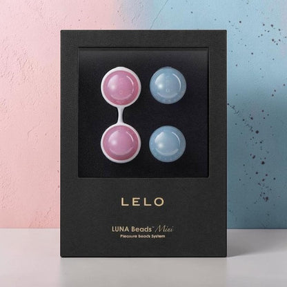 LELO Luna Beads Mini package containing four small round beach beads, two pink and two light blue, displayed inside a black box against a split pastel pink and blue background.